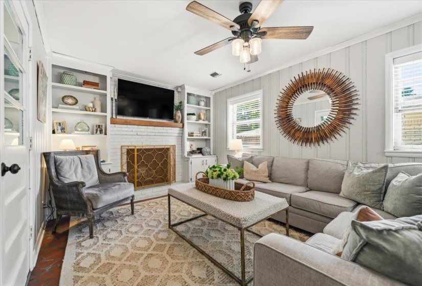 Living area featuring a white brick fireplace with a decorative screen, flanked by built-in shelving and cabinetry
