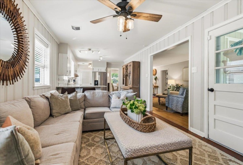 Living area featuring light wood-finish flooring, white paneling, and a ceiling fan with integrated lighting