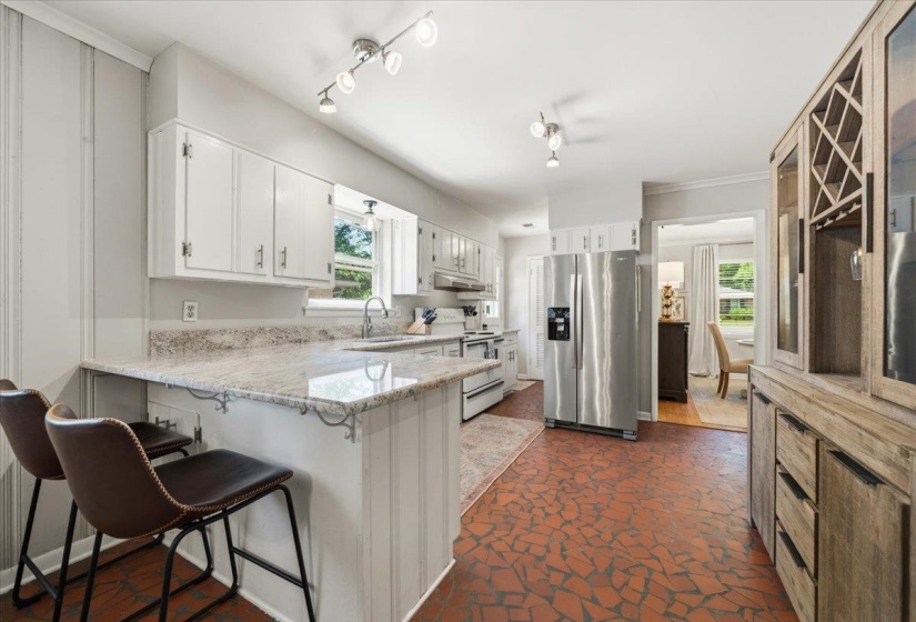 Kitchen featuring white cabinetry, light-toned countertops, stainless steel appliances, and a red mosaic tile floor