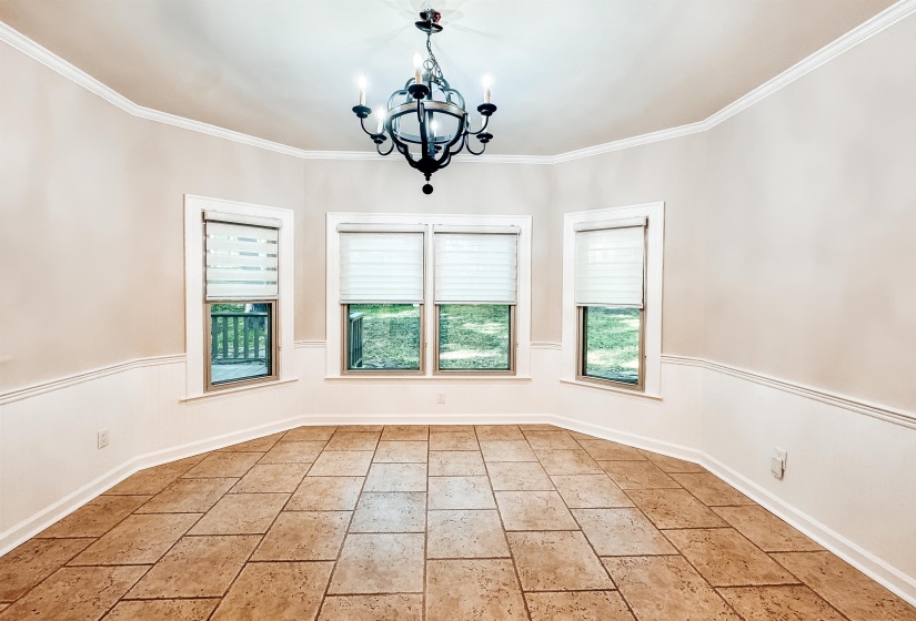 Dining area featuring ceramic tile flooring, three large windows, white wainscoting, crown molding, and a chandelier