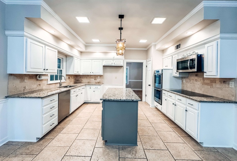 Bright kitchen featuring extensive white cabinetry, granite countertops, a central island with a contrasting base, stainless steel double ovens, and tile flooring