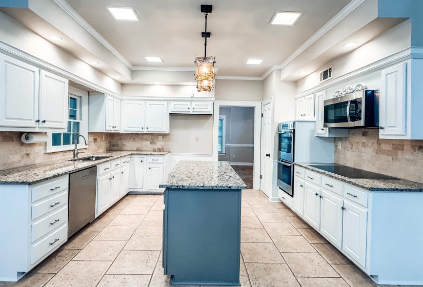 Spacious kitchen featuring white cabinetry, light-toned stone countertops, and a central island with a contrasting base