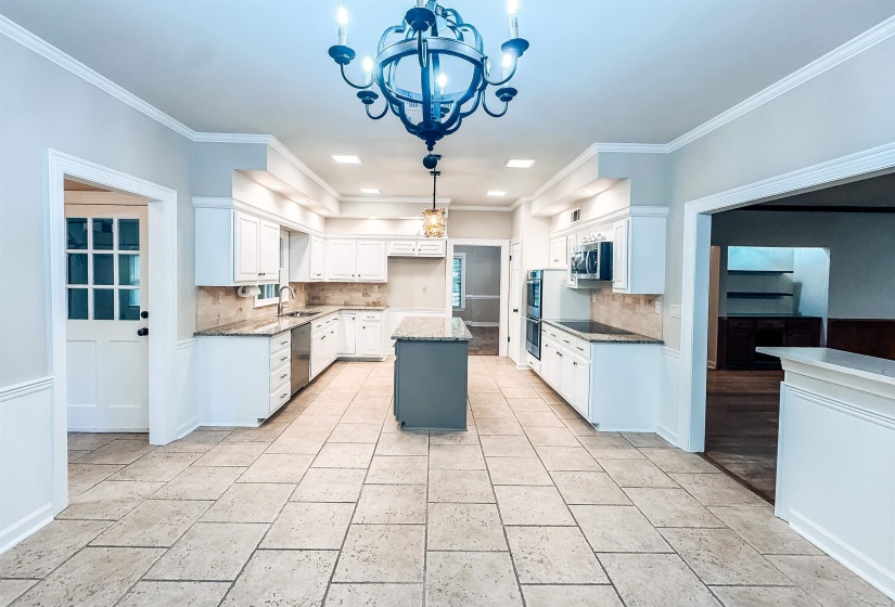 Spacious kitchen featuring an expansive tile floor, white cabinetry, granite countertops, and a central island with a contrasting base