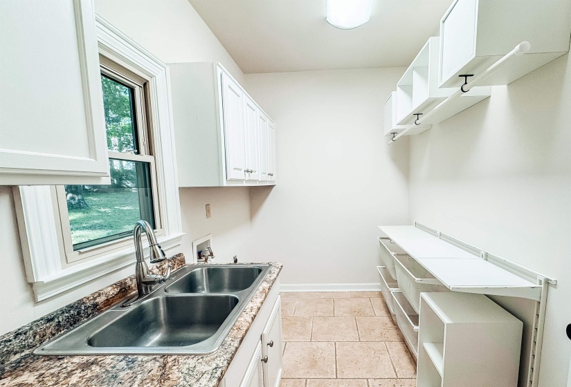 Utility room featuring a double basin stainless steel sink, a stone-finish countertop, white cabinetry, and extensive built-in shelving