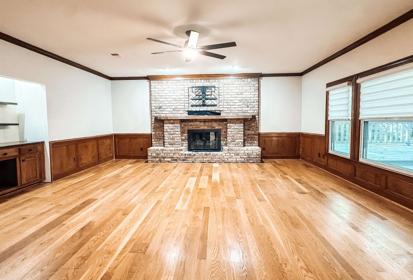 Spacious room featuring wood-finish flooring, a brick fireplace with a wood mantle, and wainscoting