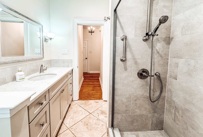 Bathroom featuring a tiled walk-in shower with glass enclosure, a single vanity with a white countertop and undermount sink, and a framed mirror