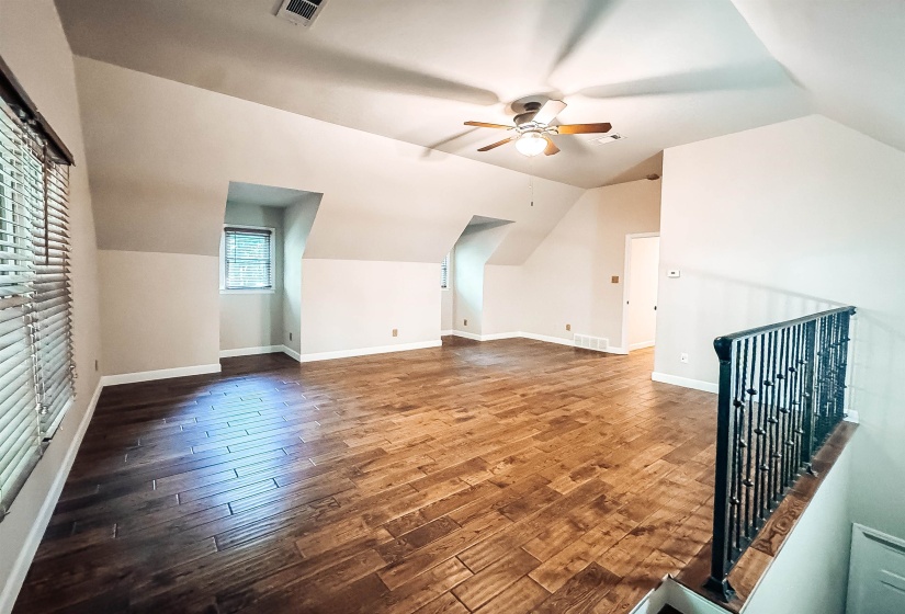 Expansive open room featuring wood-finish flooring, sloped ceilings, and a ceiling fan with light fixture