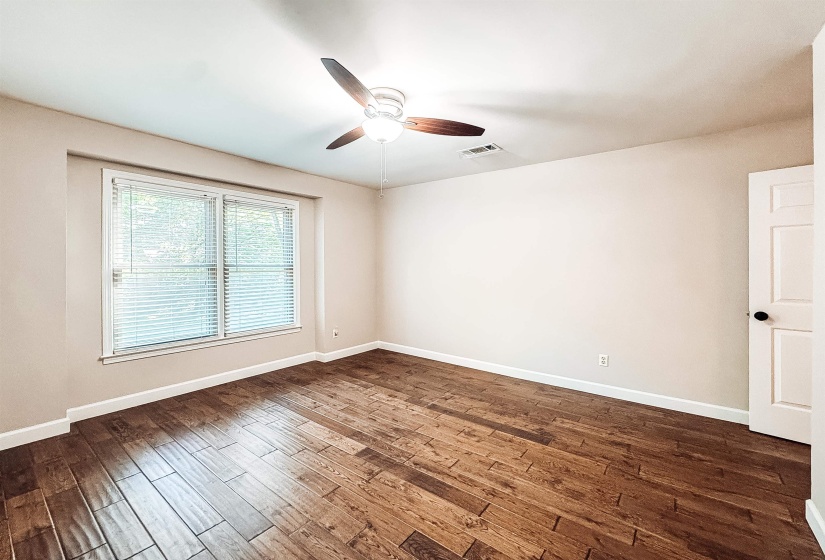 Room featuring wood-finish flooring, a ceiling fan with integrated lighting, a large window with blinds, and white trim throughout