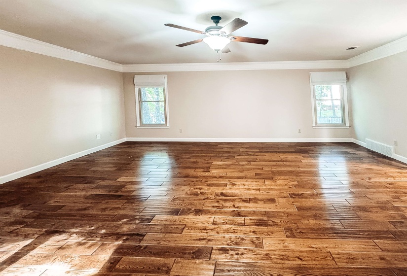 Spacious room featuring rich wood-finish flooring, two large windows with white shades, and a ceiling fan with integrated lighting