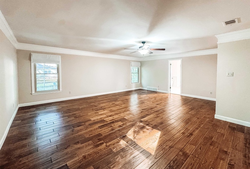 Spacious room featuring wood-finish flooring, white crown molding, a ceiling fan, and two windows with Roman shades