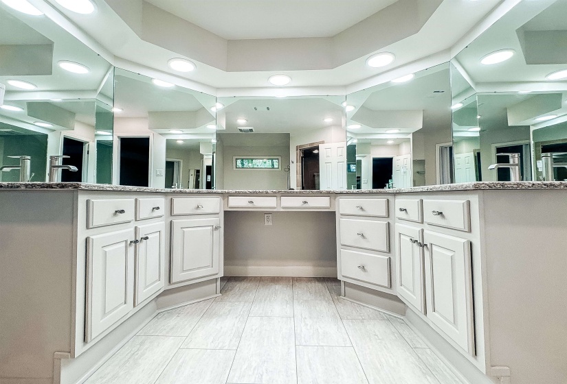 Spacious vanity area featuring twin undermount sinks with chrome faucets, a light-toned countertop, extensive wall-mounted mirrors, recessed ceiling lighting, and white wood-panel cabinetry with silver hardware