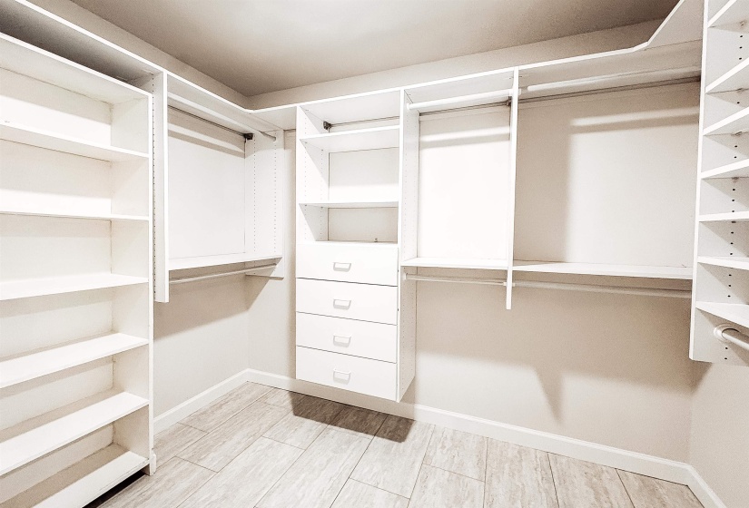 Custom walk-in closet featuring extensive built-in shelving, multiple hanging rods, four integrated drawers with chrome hardware, and wood-finish flooring
