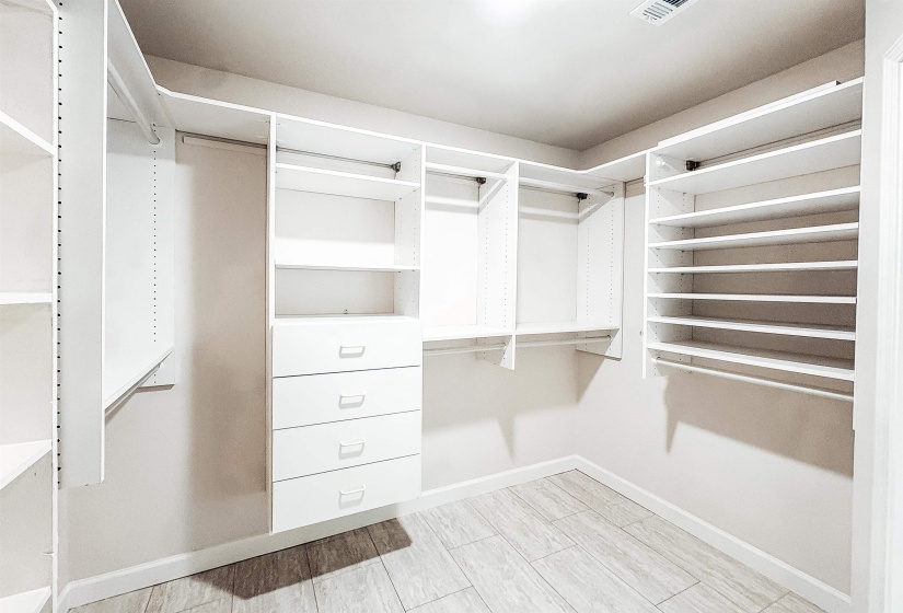 Walk-in closet featuring white built-in shelving, multiple hanging rods, four integrated drawers, and wood-finish flooring