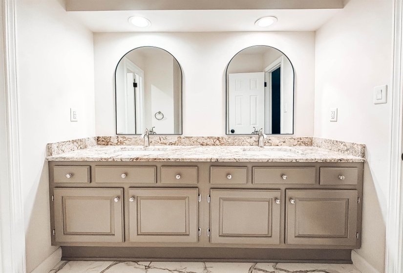 Double vanity featuring a light-toned stone countertop, dual undermount sinks with chrome fixtures, and arched mirrors