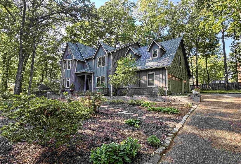 Multi-gabled exterior with vertical and horizontal siding, an integrated two-car garage, multiple dormer windows, a covered front entry, and a stone-edged driveway