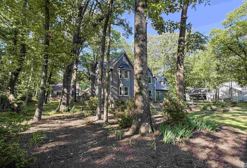 Wooded property featuring a multi-story residence with gray siding and multiple gabled roofs