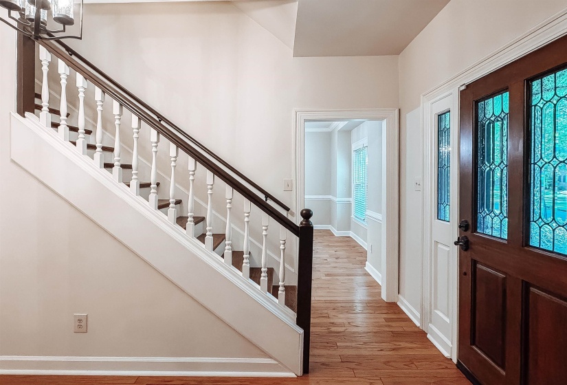Entryway featuring wood-finish flooring, a dark wood staircase with white balusters, a dark wood entry door with leaded glass panels, a white sidelight, and a decorative ceiling light fixture