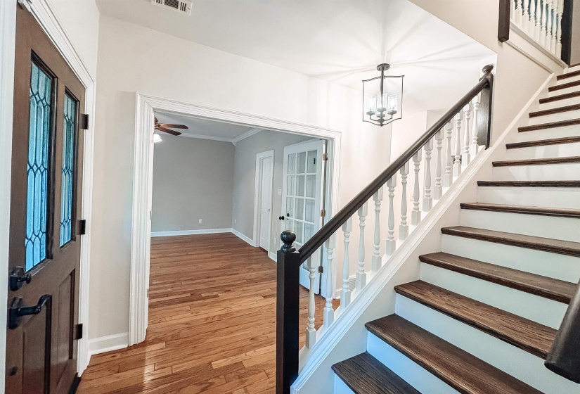 Entryway featuring a decorative glass-paneled door, hardwood flooring, a multi-tiered staircase with wood-finish treads and white risers, a white spindle railing with a dark wood-finish handrail, and an overhead lantern-style light fixture