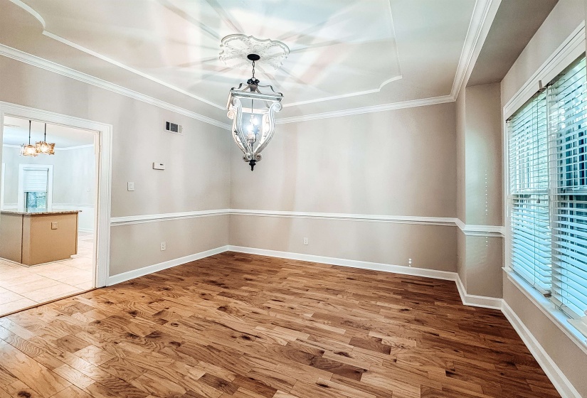 Formal dining area featuring rich wood-finish flooring, a decorative chandelier with an ornate ceiling medallion, and a tray ceiling