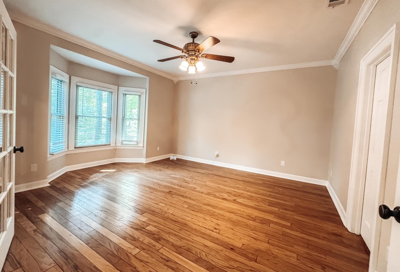 Spacious room featuring wood-finish flooring, a bay window with blinds, crown molding, and a ceiling fan with light fixture