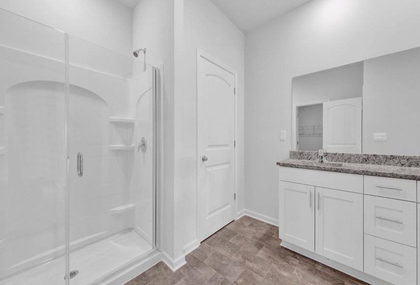 Modern bathroom featuring a glass-enclosed shower with integrated shelving, a spacious vanity with white cabinetry, a large wall-mounted mirror, a stone-finish countertop, and wood-finish flooring