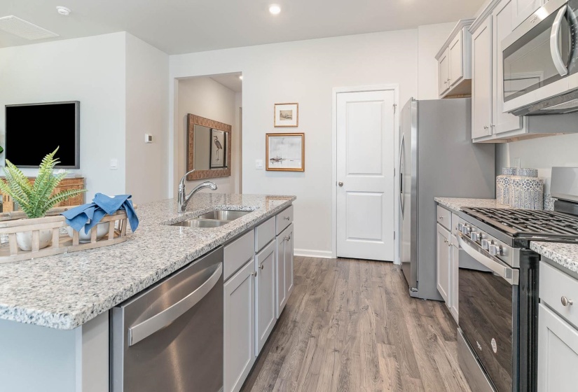 Open-concept kitchen featuring light-toned cabinetry, stainless steel appliances, a double basin sink, expansive stone countertops, and wood-finish flooring