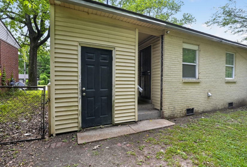 Exterior featuring a black paneled door, light-colored vinyl siding, and brick facade
