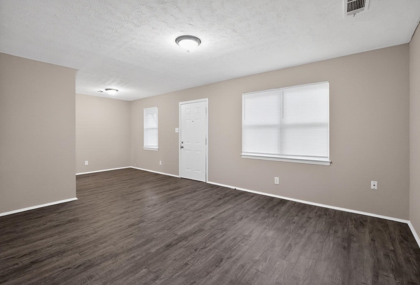 Spacious room featuring wood-finish flooring, neutral-toned walls, multiple windows with blinds, and white trim throughout