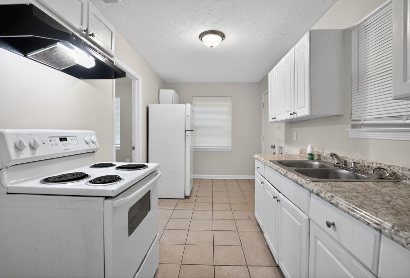 Kitchen featuring white cabinetry, a double basin sink, light-toned countertops, and tile flooring