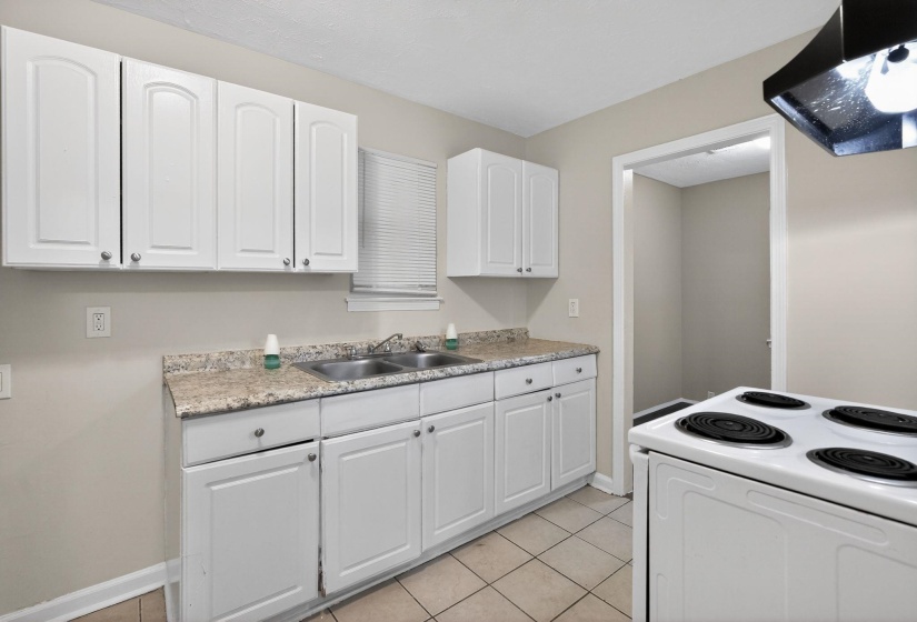 Well-lit kitchen with white shaker-style cabinetry, a dual basin stainless steel sink, and a speckled countertop