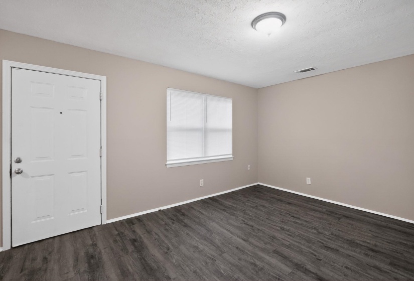 Spacious room featuring wood-finish flooring, neutral-toned walls, and a large window with privacy blinds