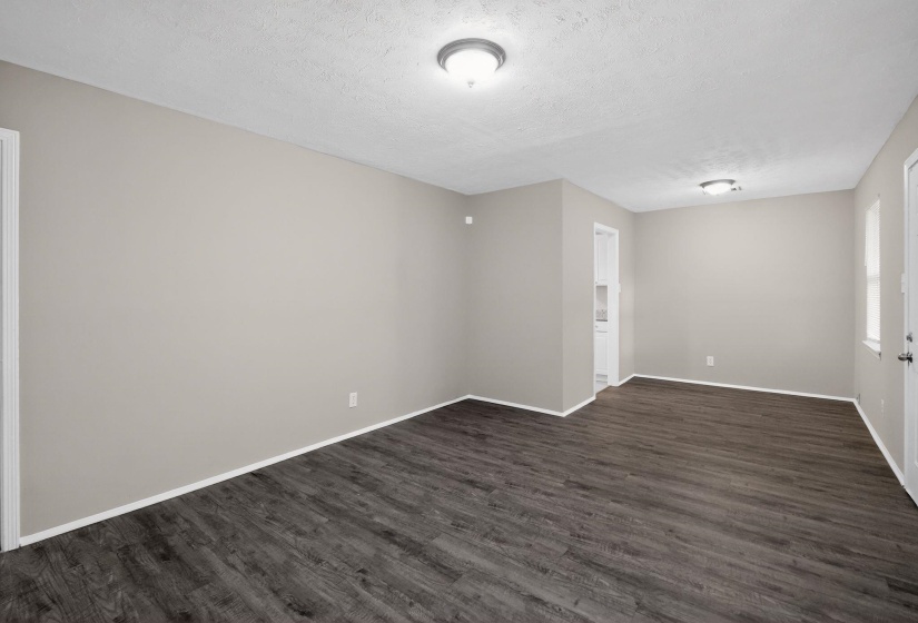 Spacious room featuring wood-finish flooring, neutral-toned walls, white baseboards, and ceiling-mounted flush lighting