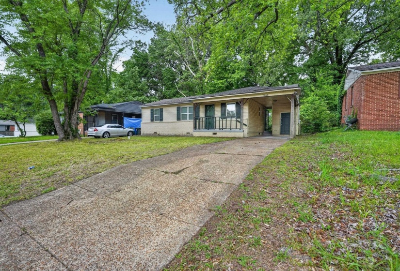Single-story residence featuring a covered carport, front porch with metal railing, and a concrete driveway