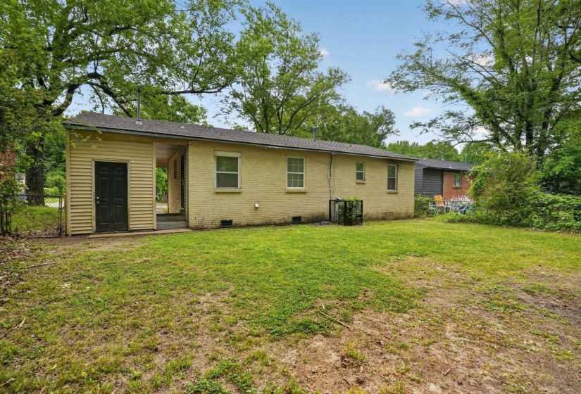 Expansive rear yard featuring green lawn space, mature perimeter trees, and a brick exterior home with multiple windows and a covered entrance
