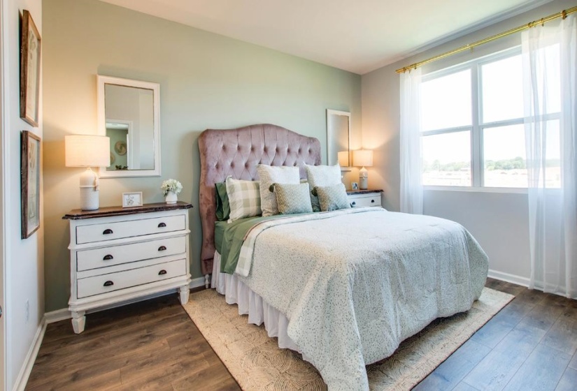 Bedroom featuring wood-finish flooring, light green wall paint, and a large window with white trim