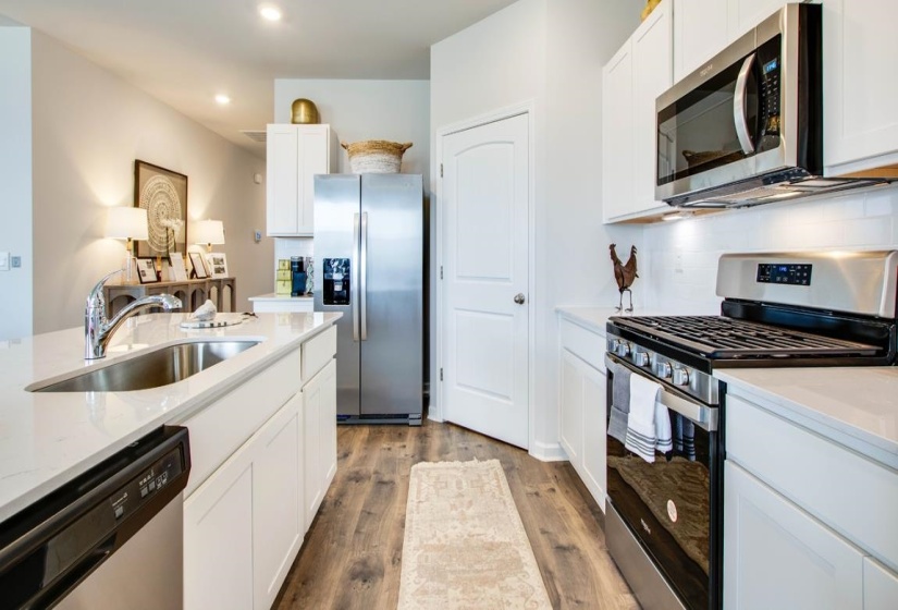 Kitchen featuring white cabinetry, light countertops, wood-finish flooring, stainless steel appliances, and a subway tile backsplash