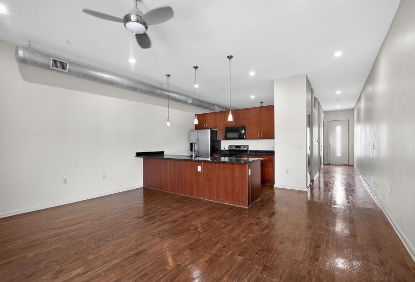 Open-concept living space featuring wood-finish flooring, a kitchen island with stone countertop, stainless steel appliances, and a ceiling fan