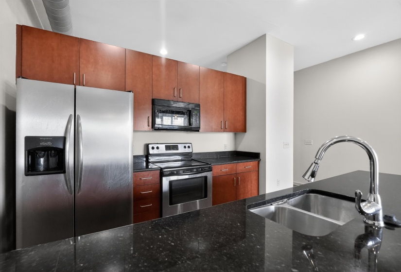 Kitchen featuring dark stone countertops, stainless steel appliances, a double basin sink with a high-arc faucet, and cherry-toned cabinetry
