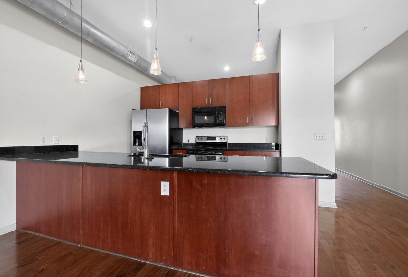 Kitchen featuring a dark wood-finish island with a contrasting dark countertop, matching upper cabinetry, stainless steel appliances, and pendant lighting