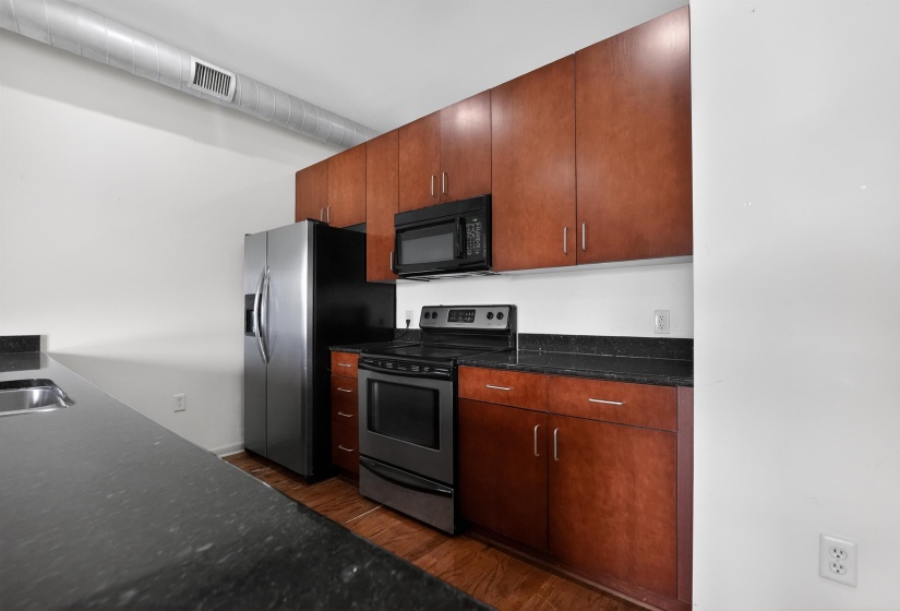 Modern kitchen featuring dark wood cabinetry, a stainless steel refrigerator, stainless steel range with black oven, black microwave, and dark countertops