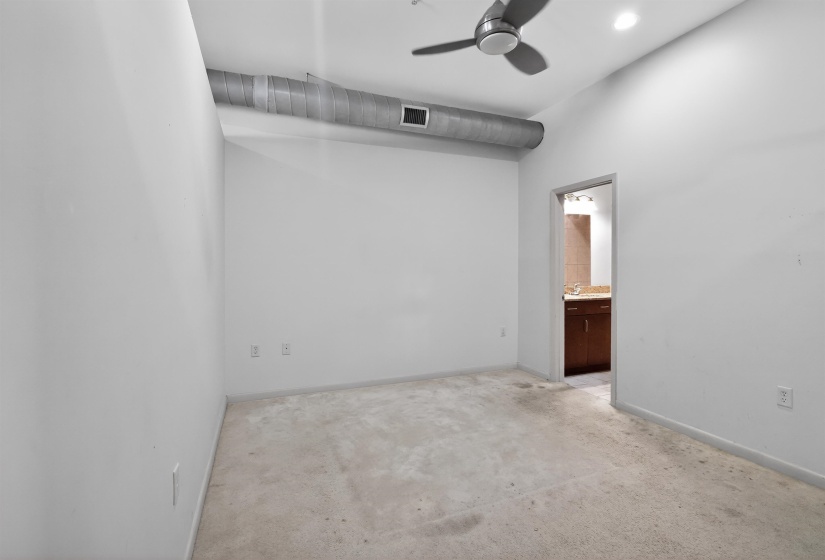Spacious room with high ceilings, exposed ductwork, a ceiling fan with integrated lighting, and an entryway to an adjoining bathroom