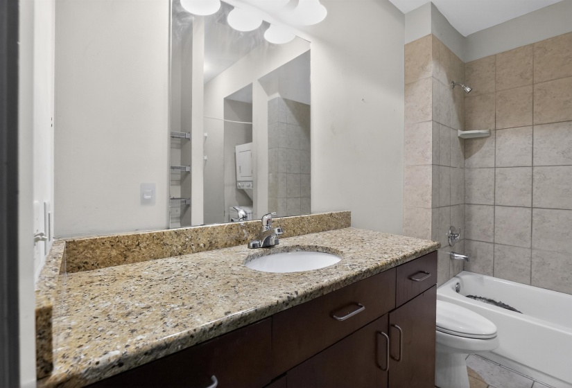 Bathroom featuring a wood-finish vanity with an integrated sink and a speckled countertop, a large wall-mounted mirror, and a shower-over-tub combination with tiled walls