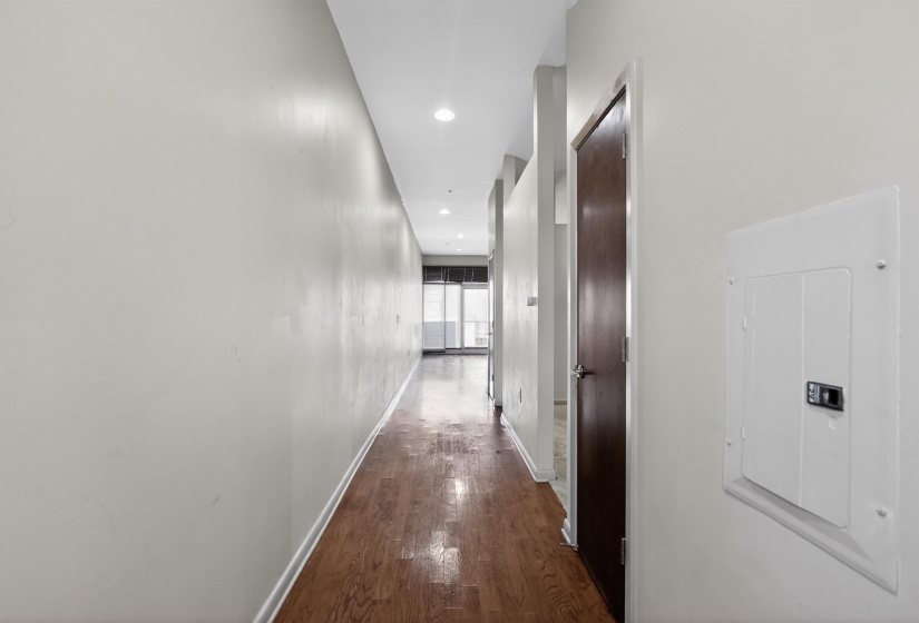 Hallway featuring wood-finish flooring, recessed lighting, white walls, and a dark wood-finish door