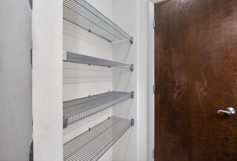 Interior storage closet featuring multiple wire shelving units and a stained wood-finish door with brushed chrome hardware