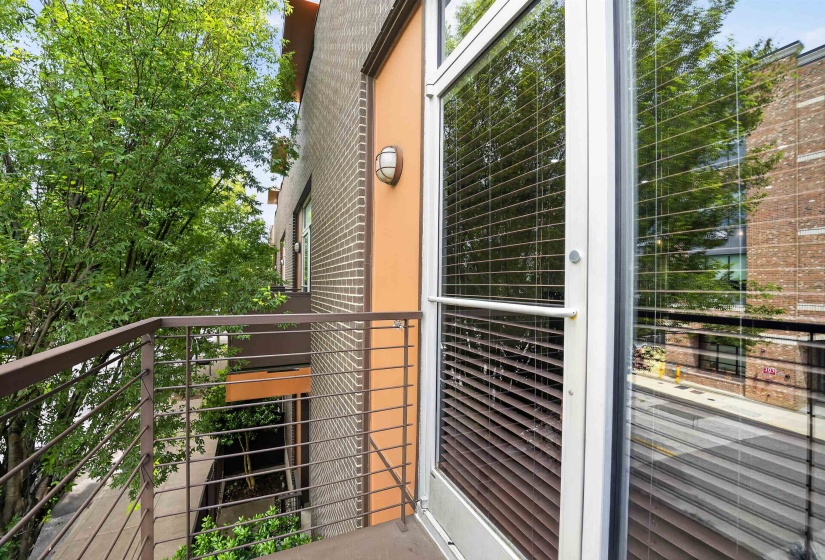 Balcony featuring metal railings, a full-light door with horizontal blinds, and a sconce light fixture