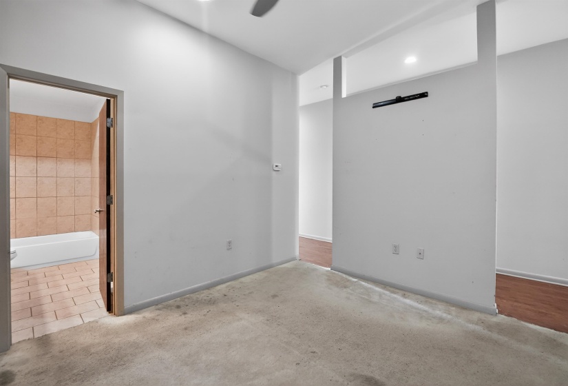 Carpeted room featuring a white interior wall, a partial divider wall, and an open doorway revealing a bathroom with tile flooring and a bathtub