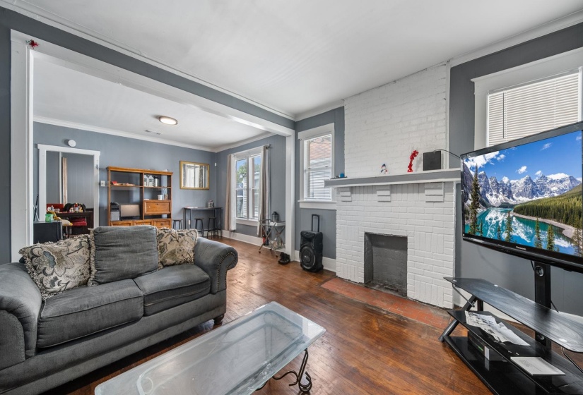 Living area featuring wood-finish flooring, white painted brick fireplace surround with mantel, white trim, and gray wall paint
