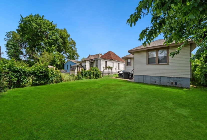 Expansive backyard featuring a manicured lawn, established perimeter foliage, and a vinyl-sided exterior with dual windows