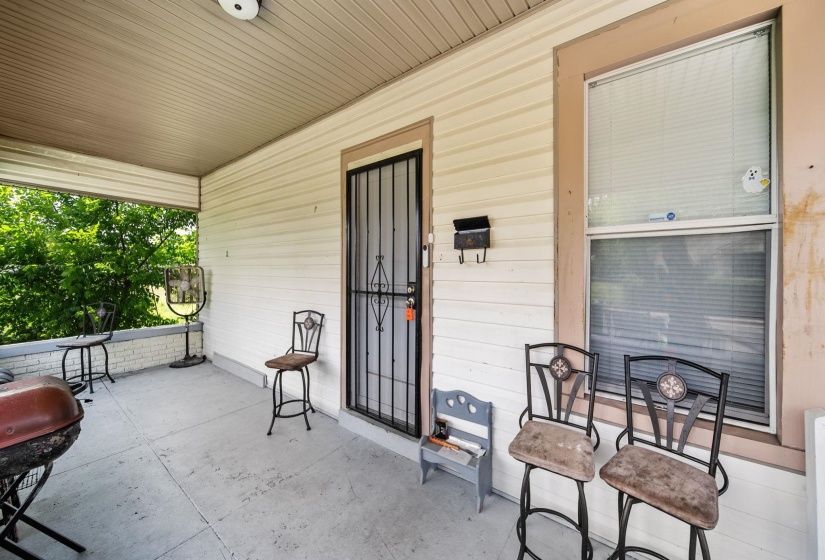 Covered front porch featuring a security screen door, large window with blinds, and durable siding
