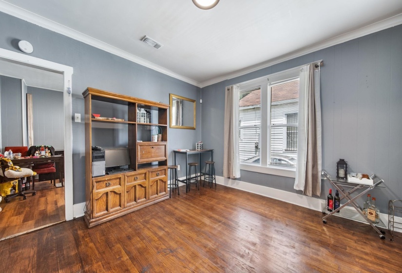 Spacious room featuring wood-finish flooring, light gray walls, white baseboards, and crown molding